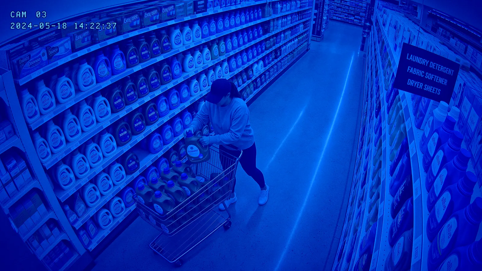 A security camera view of a shopper loading laundry detergent into a shopping cart.